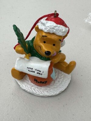 This vintage 1990s Disney Store Christmas ornament features Winnie the Pooh wearing a Santa hat and writing a letter while sitting on a "Hunny" pot
